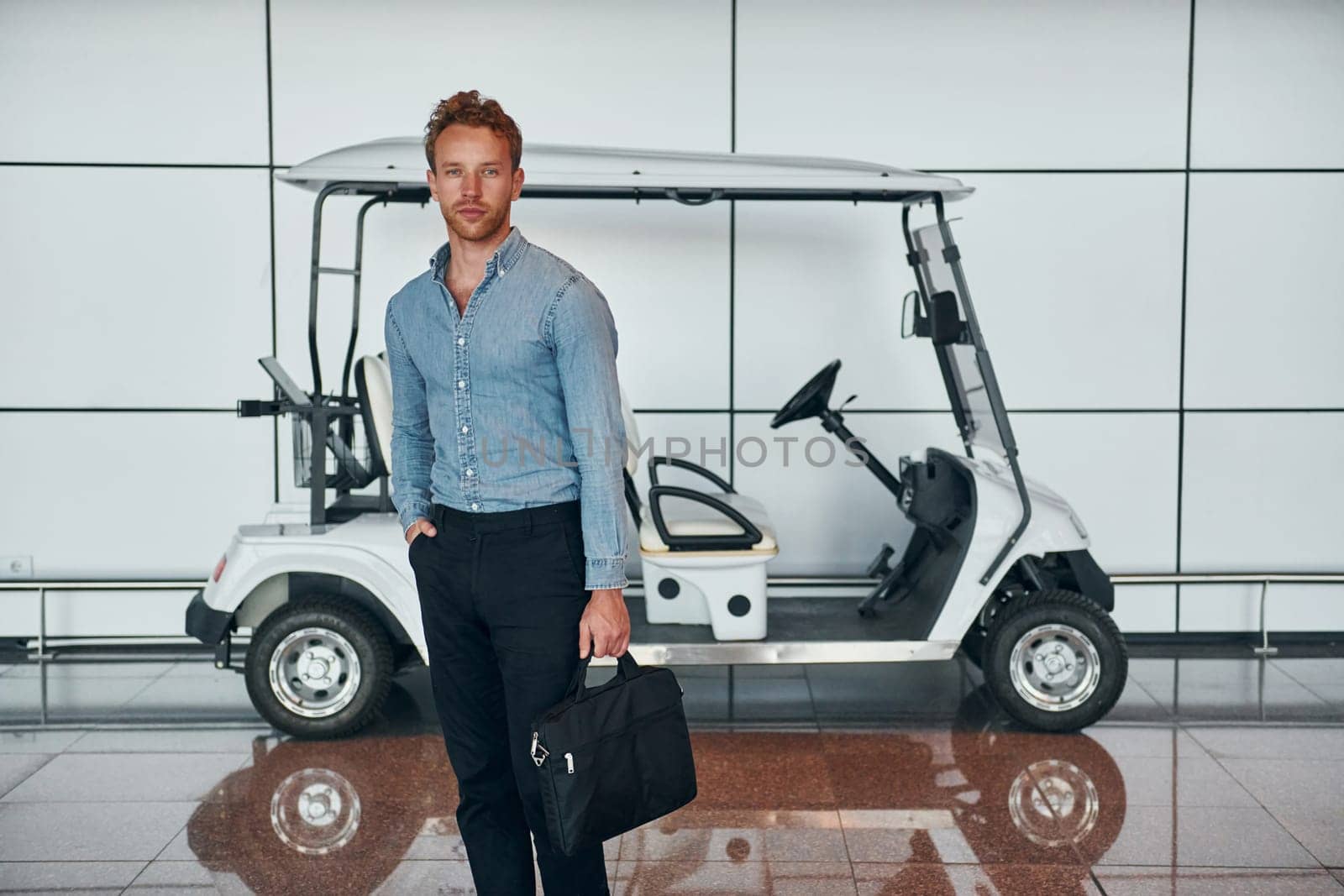 Against vehicle. Young man in formal wear is in modern airport. Conception of vacation.