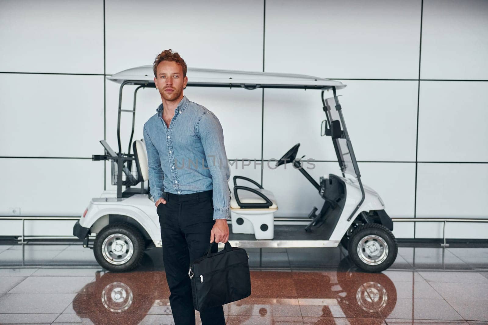 Against vehicle. Young man in formal wear is in modern airport. Conception of vacation.