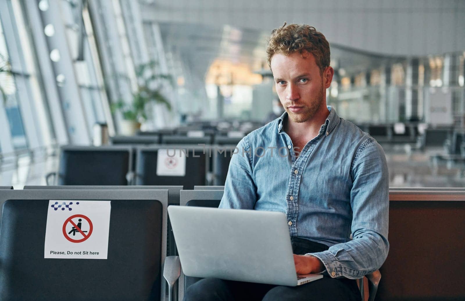 Sitting inside. Young man in formal wear is in modern airport. Conception of vacation by Standret