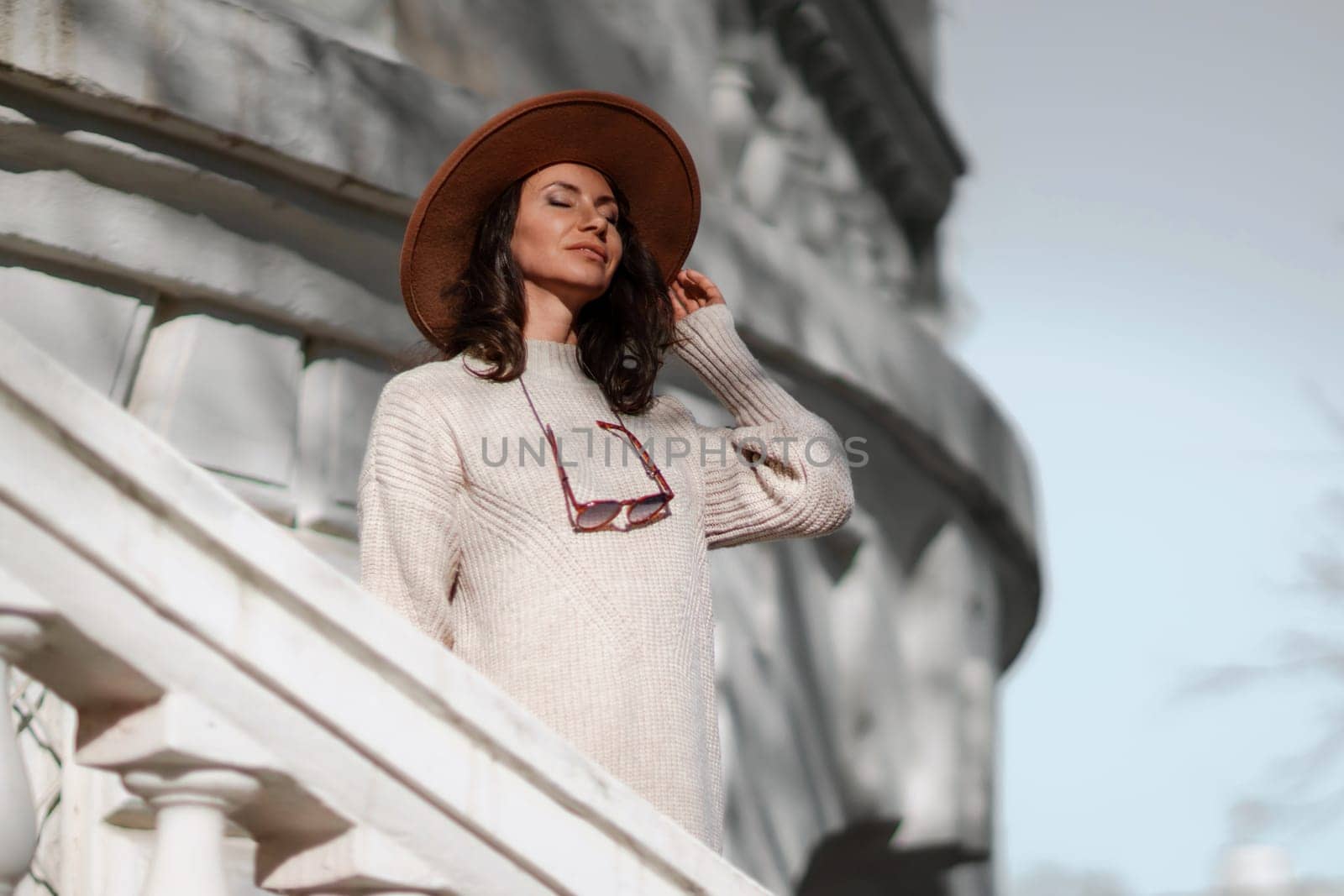 Woman walks in the city, lifestyle. Young beautiful woman in a loose light sweater, brown skirt and sneakers with a hat