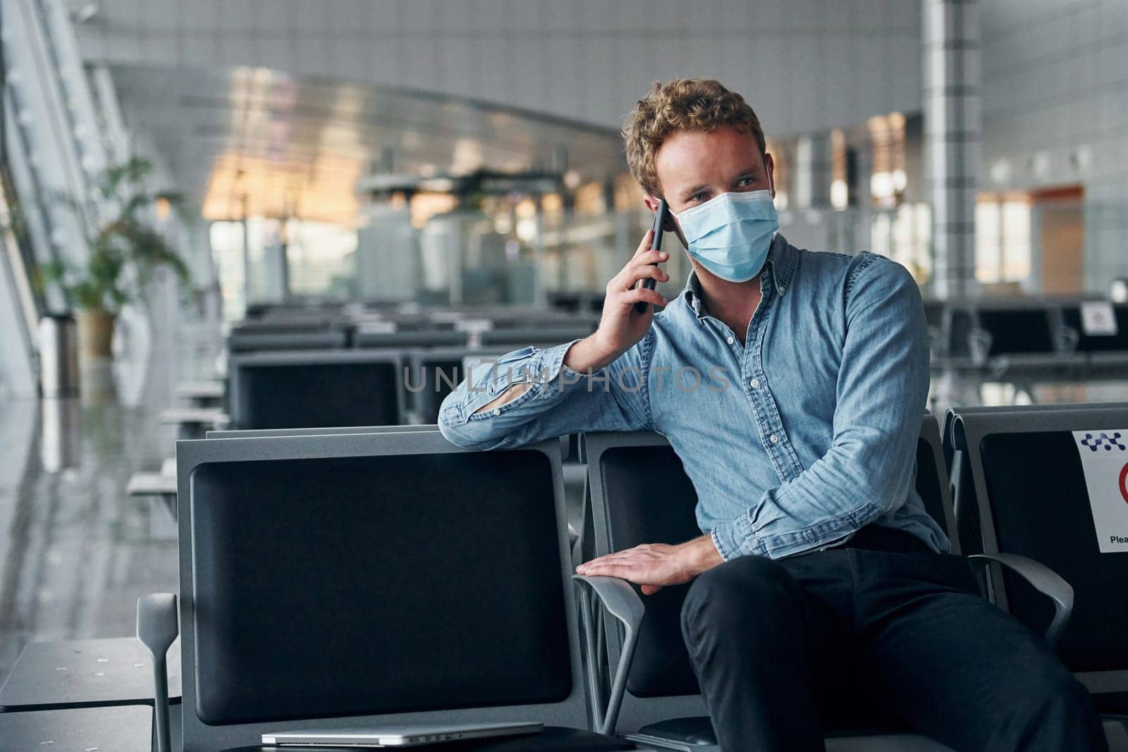 Sitting inside. Young man in formal wear is in modern airport. Conception of vacation.