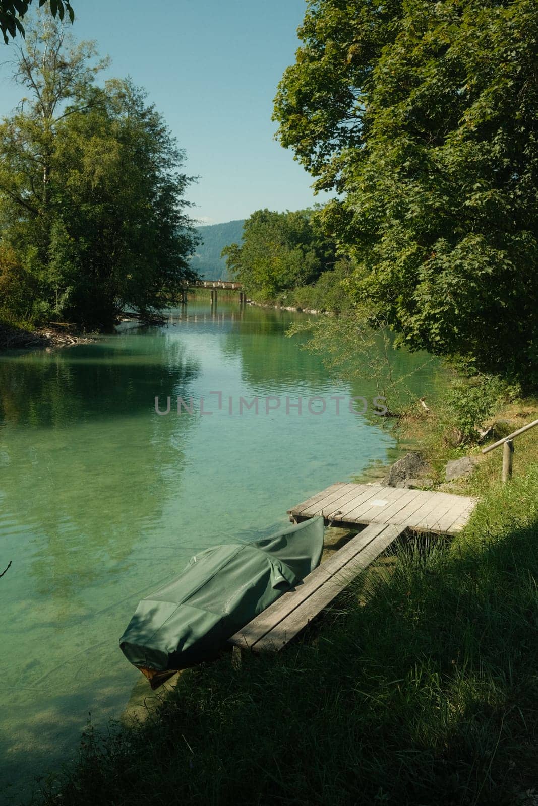 Jetty with a covered boat beside it near the crystal-clear water at the Mangfall river in Germany