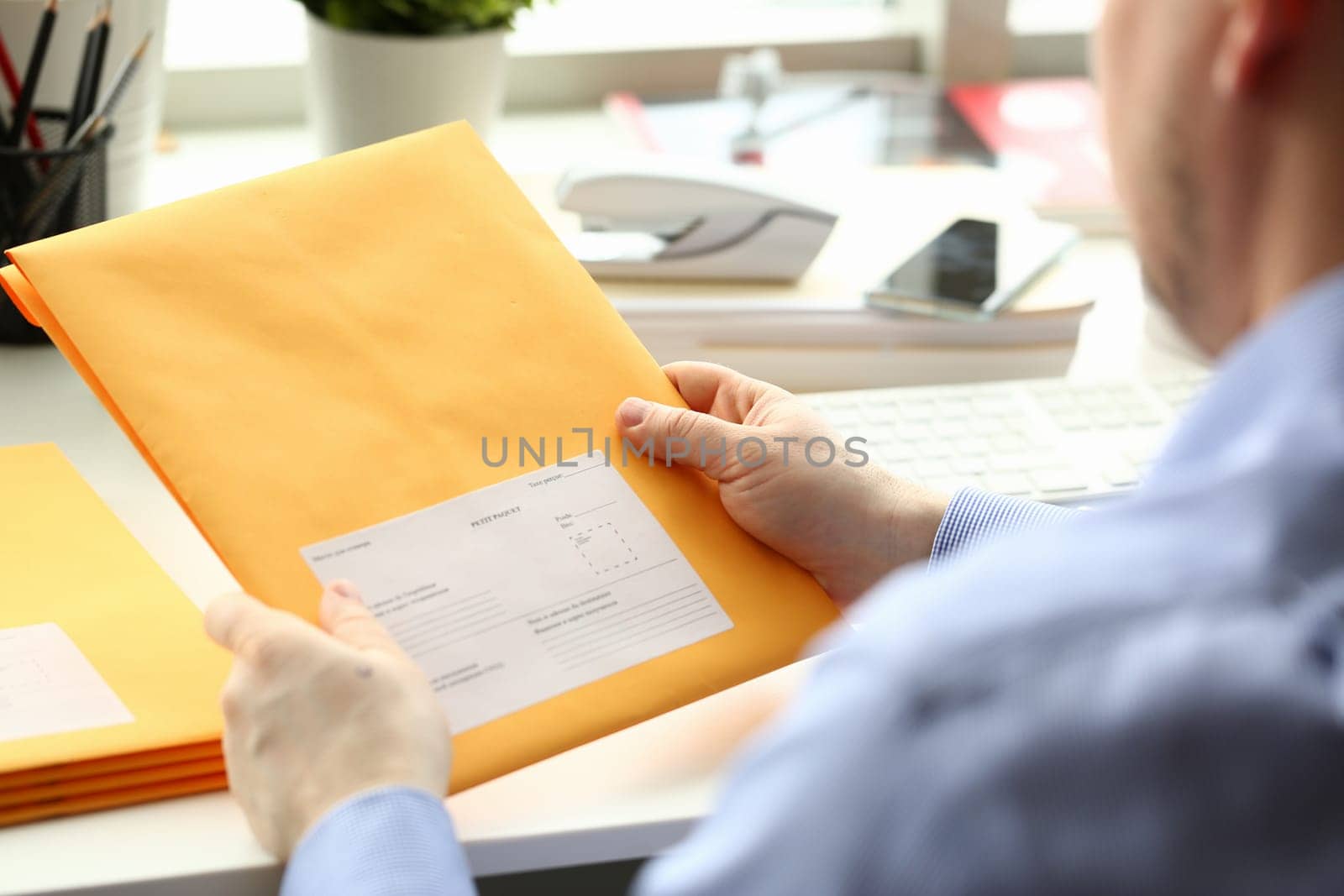 Businessman holding yellow package with mail in office. Delivery or mailing business mail concept