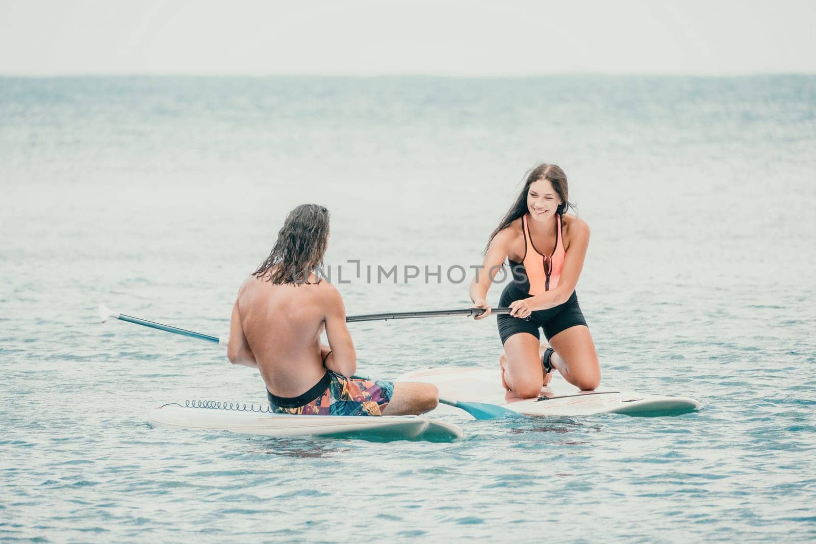 Sea woman and man on sup. Silhouette of happy young woman and man, surfing on SUP board, confident paddling through water surface. Idyllic sunset. Active lifestyle at sea or river