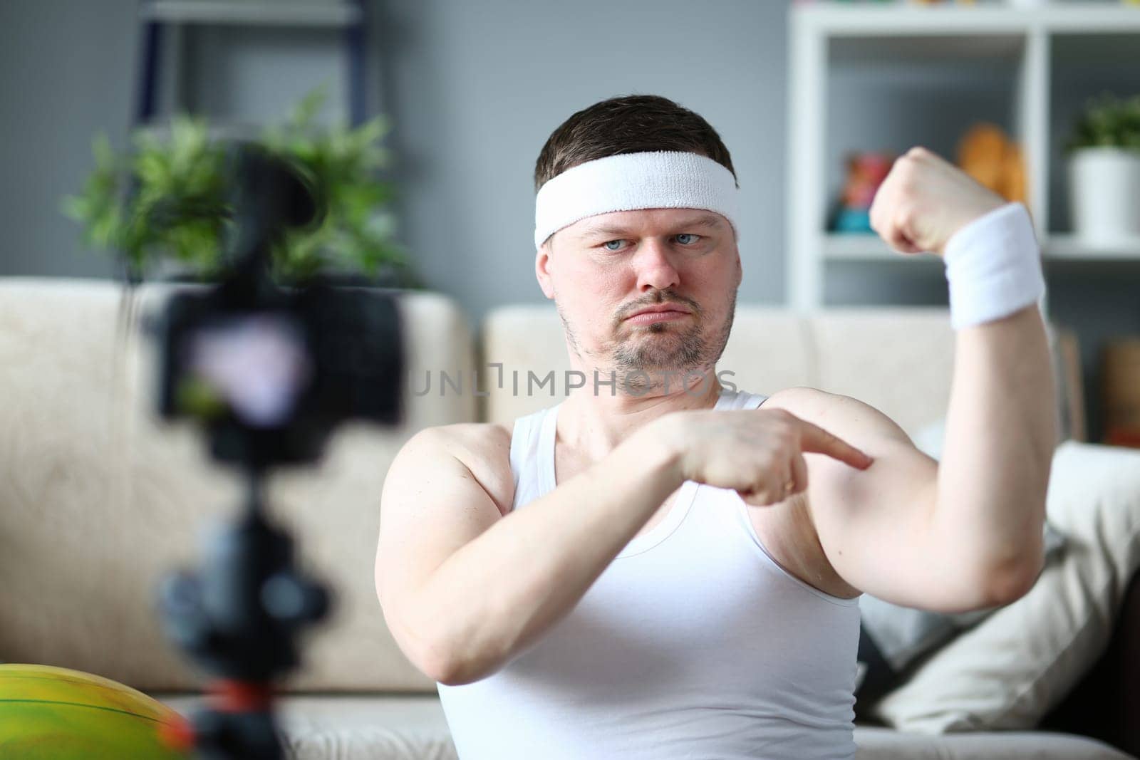 Energetic joyful male blogger measuring bicep size while smiling and updating blog. Big biceps and home fitness concept
