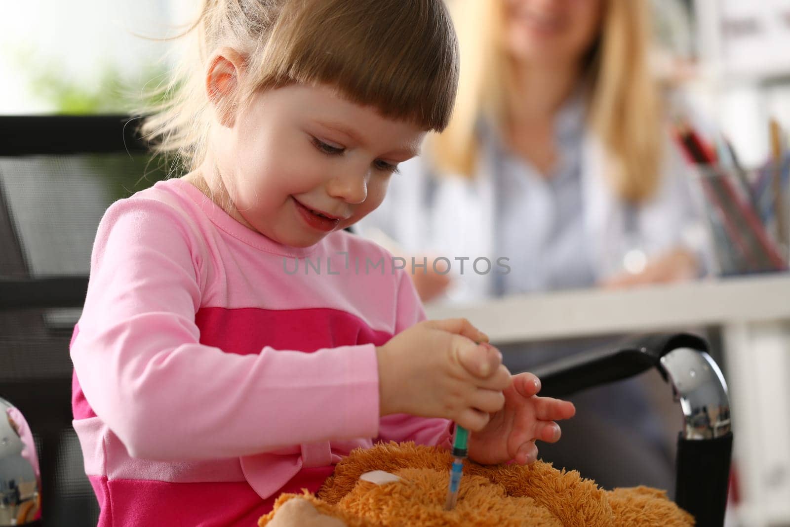 Little girl child makes injection to toy in doctor office. Baby health insurance and assistance pediatrician concept