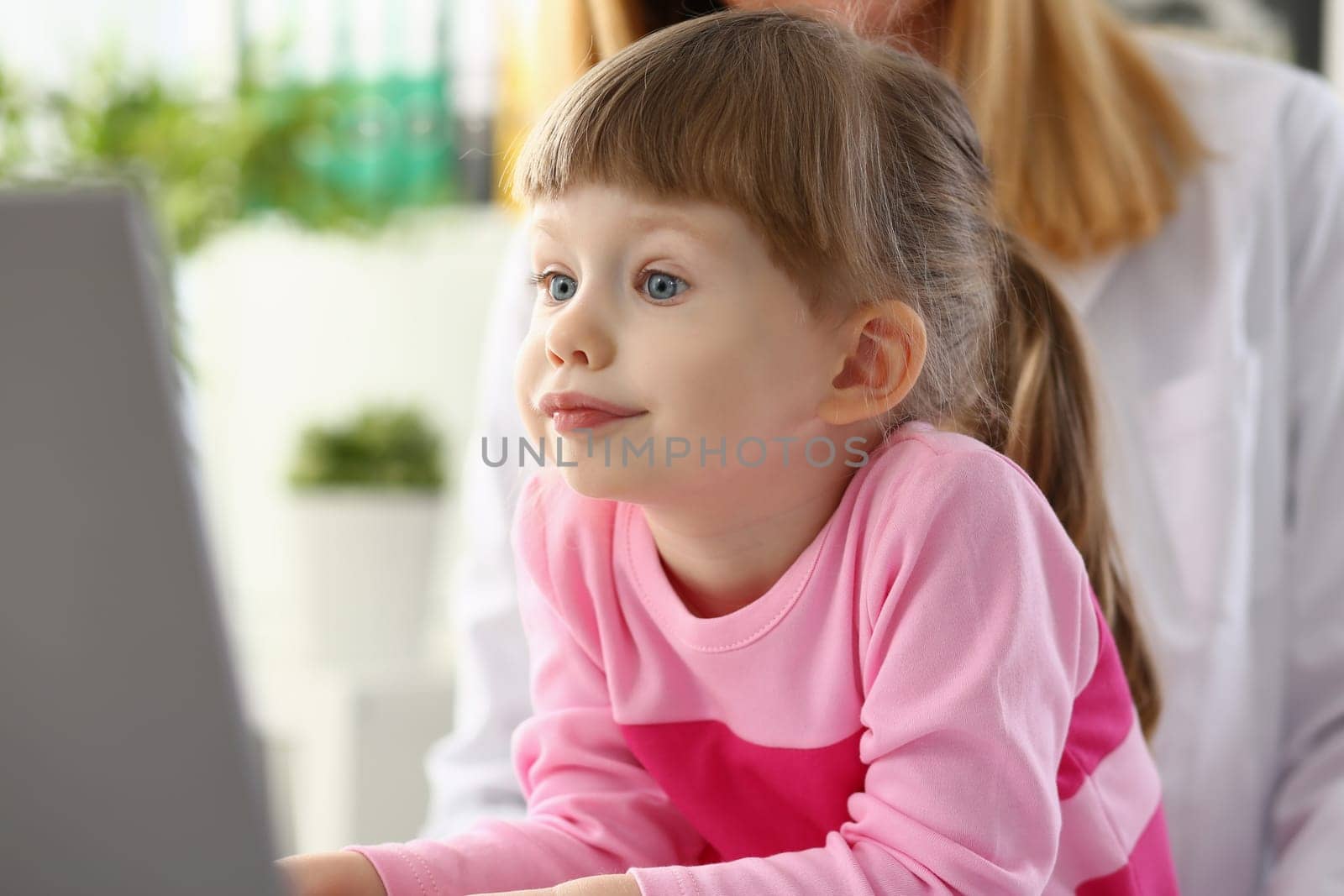 Beautiful little girl child carefully looks at monitor screen by kuprevich