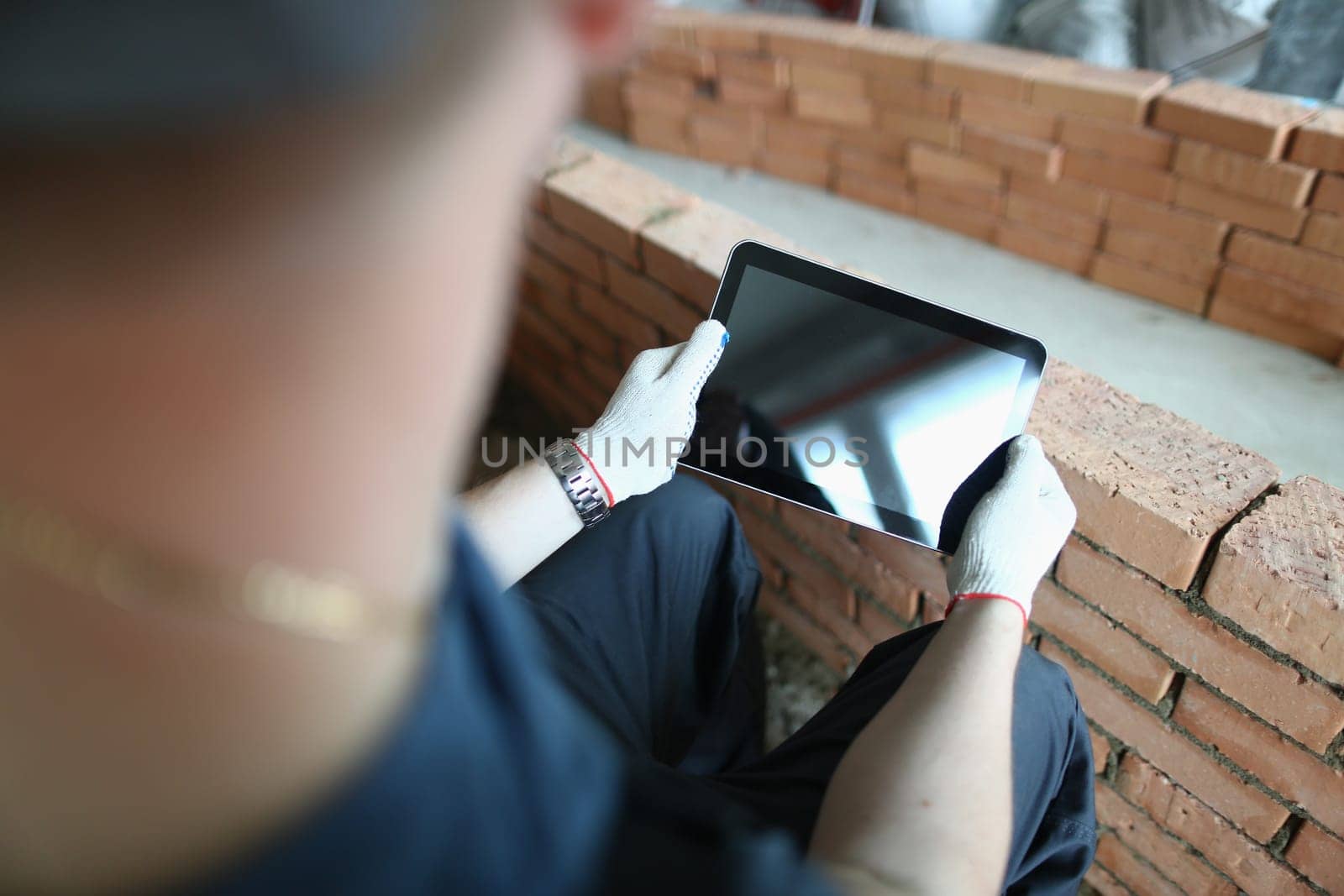 Builder stands in house under construction and holds tablet computer. Mobile applications for self-repair at home concept