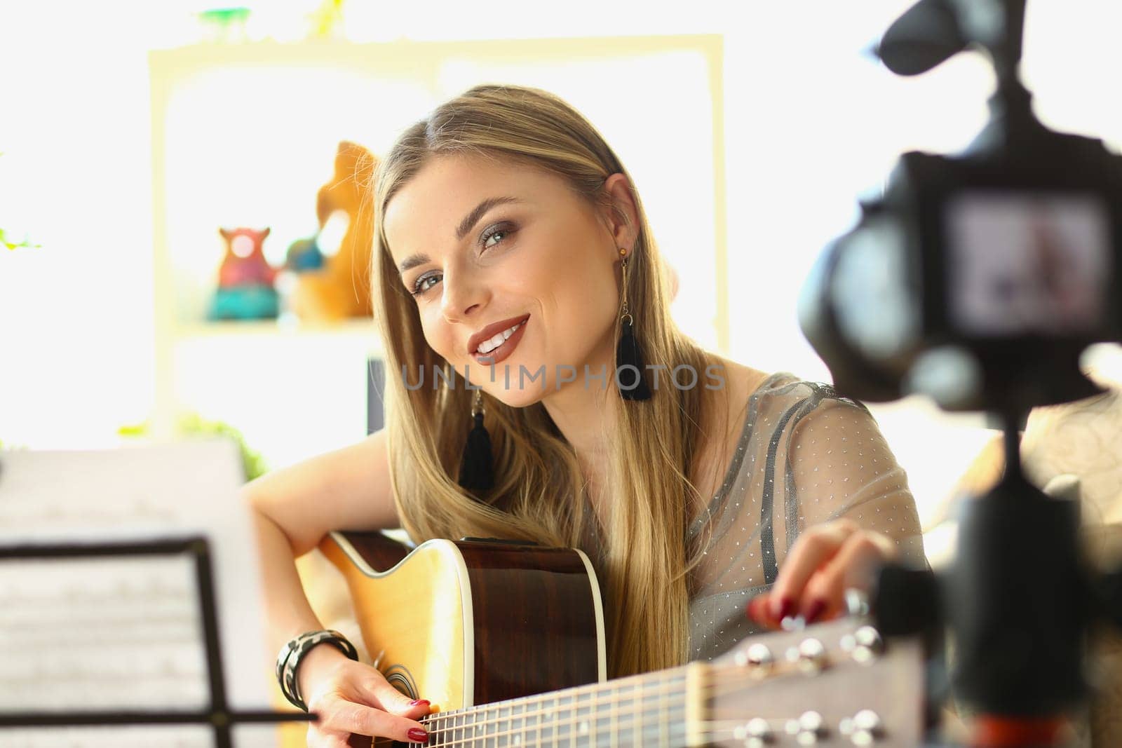 Blonde woman playing guitar live on camera. Girl leads a music video blog concept