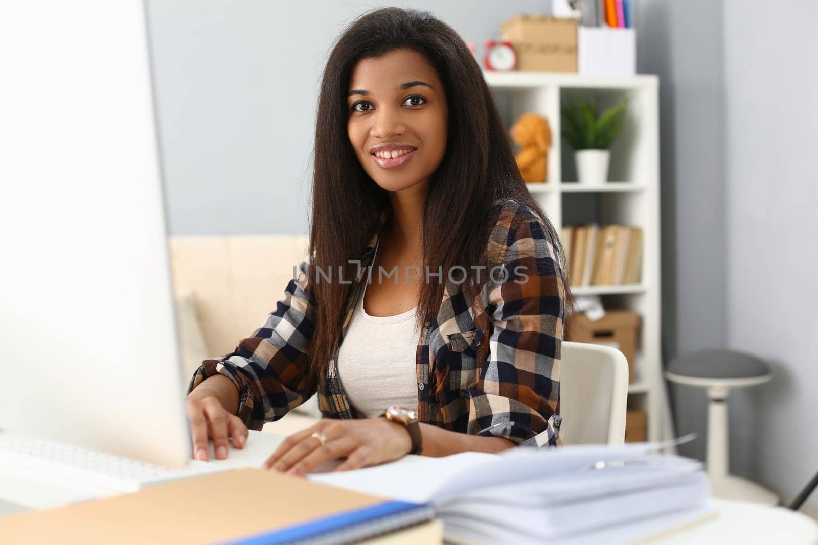 Portrait of beautiful smiling african american office worker sitting at desk and using computer by kuprevich