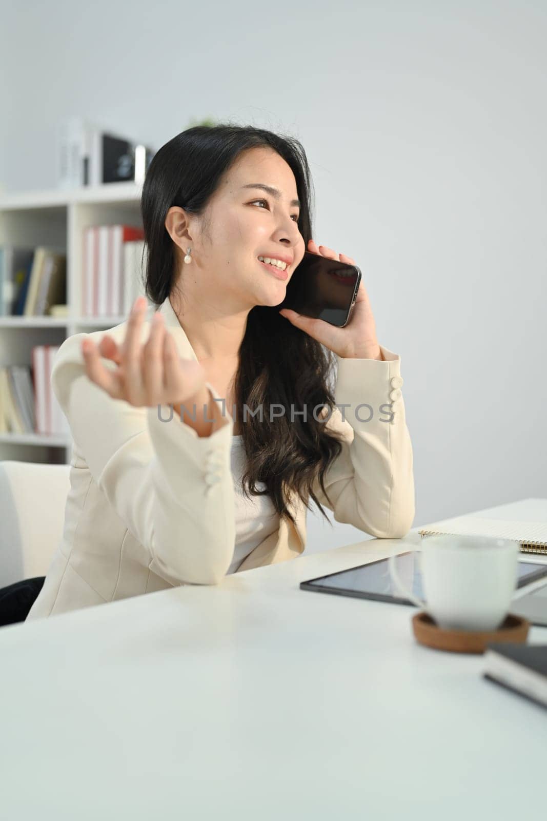 Portrait of smiling corporate CEO woman sitting in modern office and talking on mobile phone by prathanchorruangsak