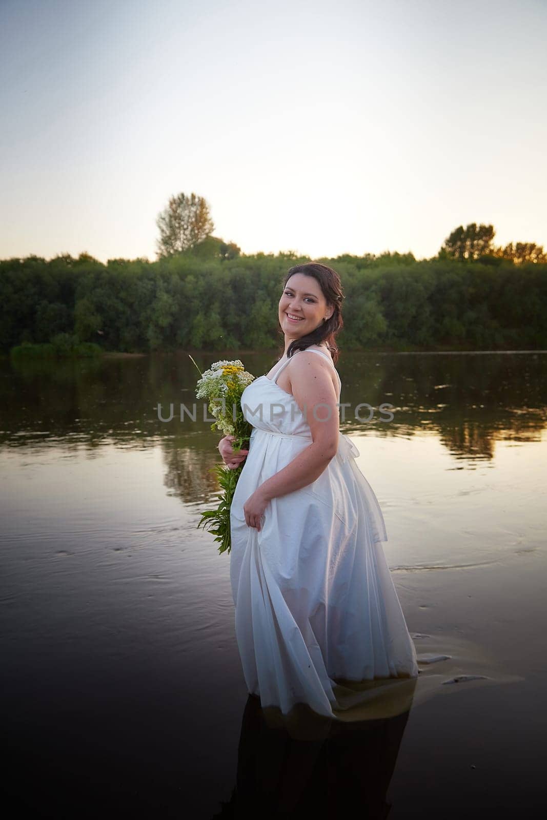 Slavic plump plump chubby girl in long white dress on the feast of Ivan Kupala with flowers and water in a river or lake on a summer evening by keleny