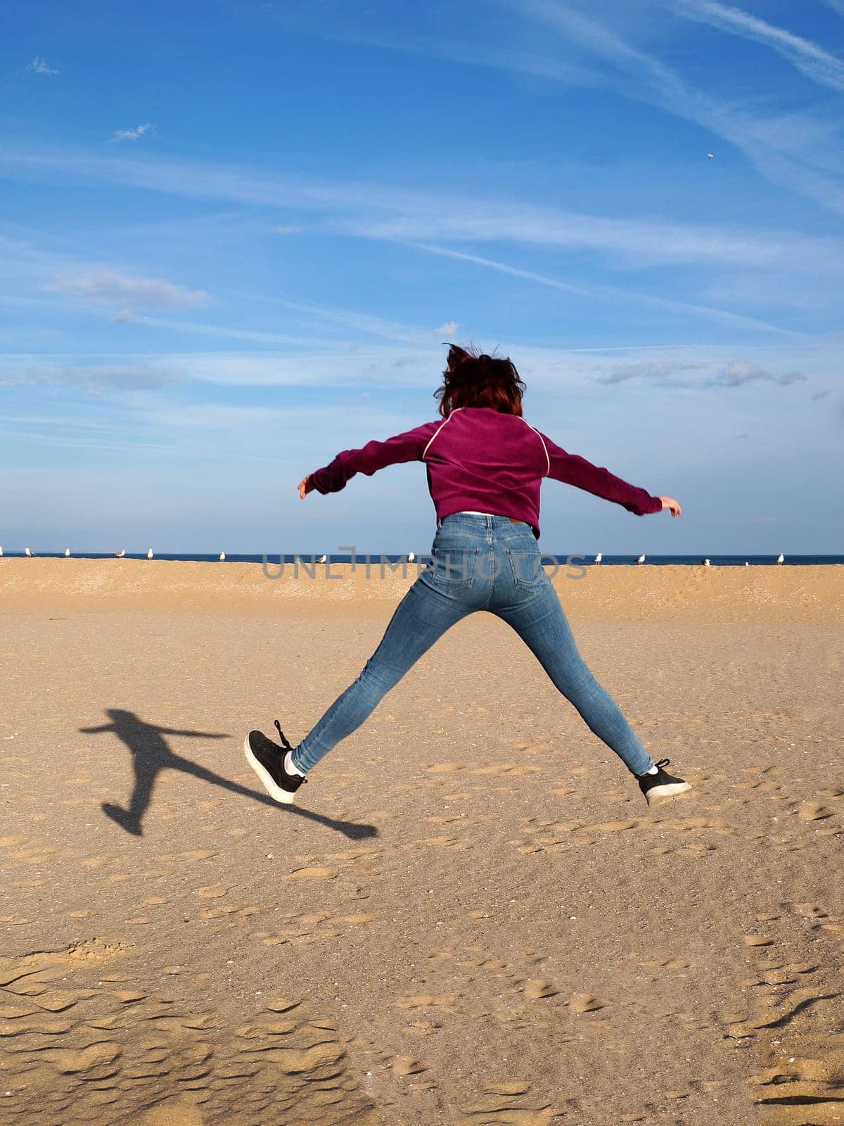 red-haired teen girl jumping with her arms and legs outstretched, rear view.