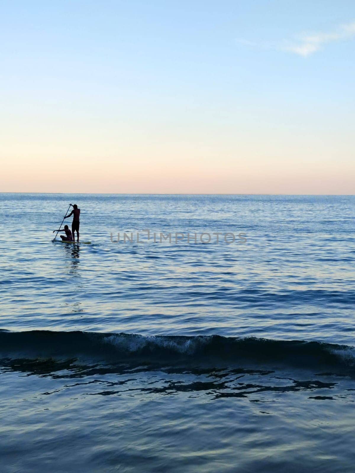 silhouette of a man and a woman sailing on a supboard in the sea at sunset.