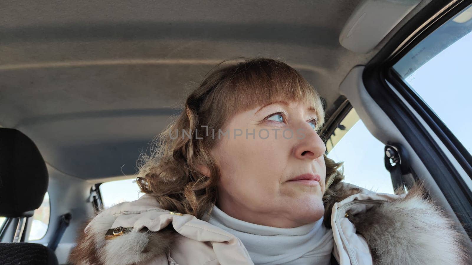 Woman sitting in the car in road trip. Blonde senior Woman driving transport. Lady travelling in cold time