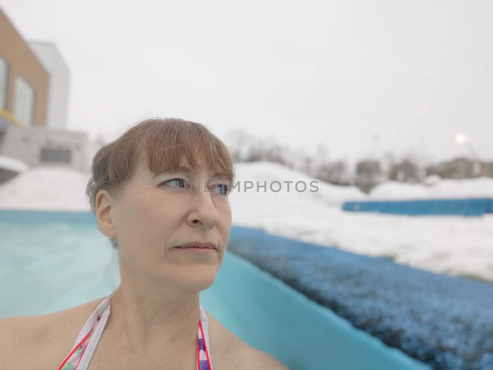 Adult mature woman takes selfie in a pool with warm hot termal mineral water in winter and white snow around. Wellness center and the concept of health care. Travel, recreation, medicine and rest