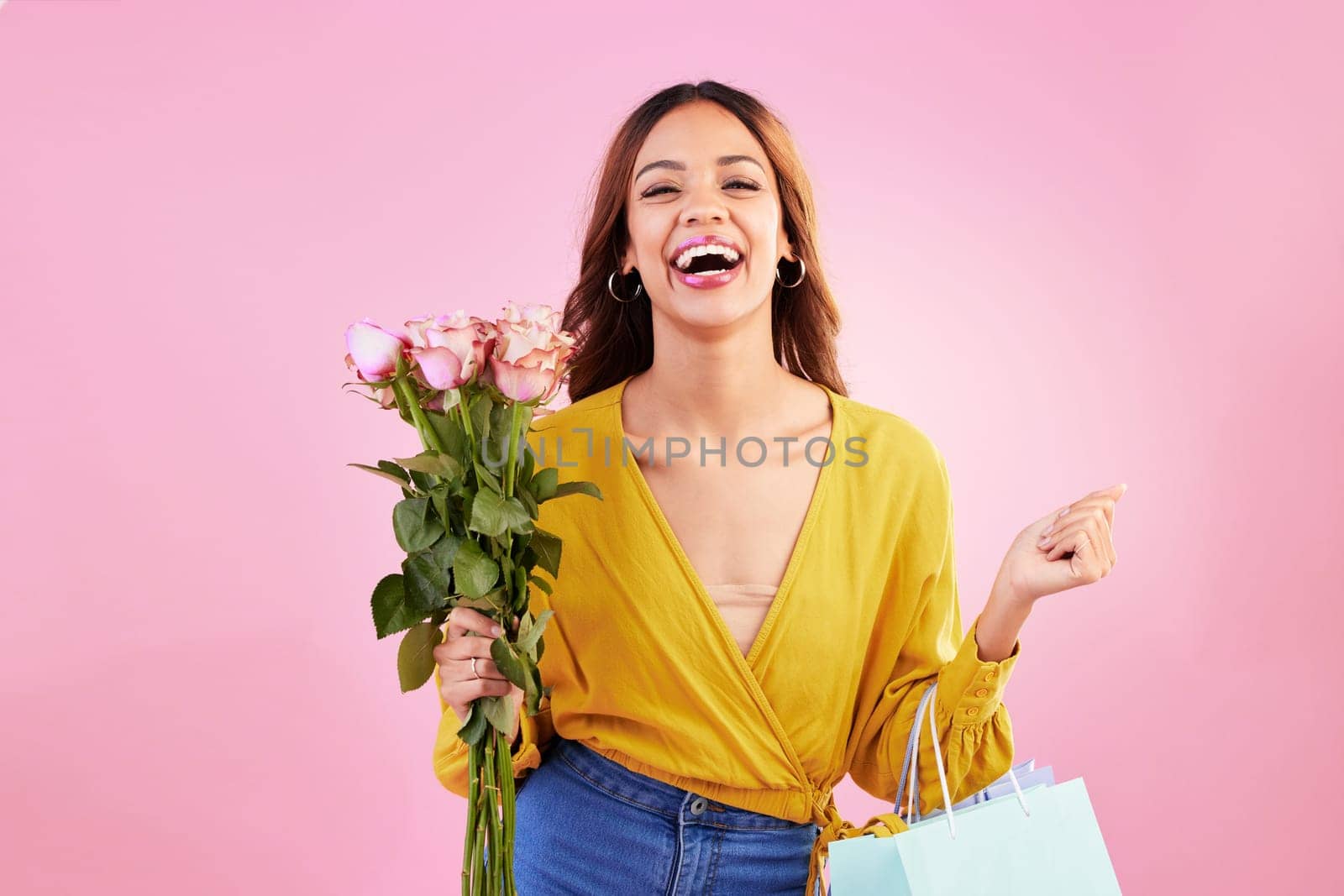 Happy, shopping bags and flowers with woman in studio for retail, birthday and spring. Event, party and celebration with female customer and roses on pink background for sale, discount and romance.