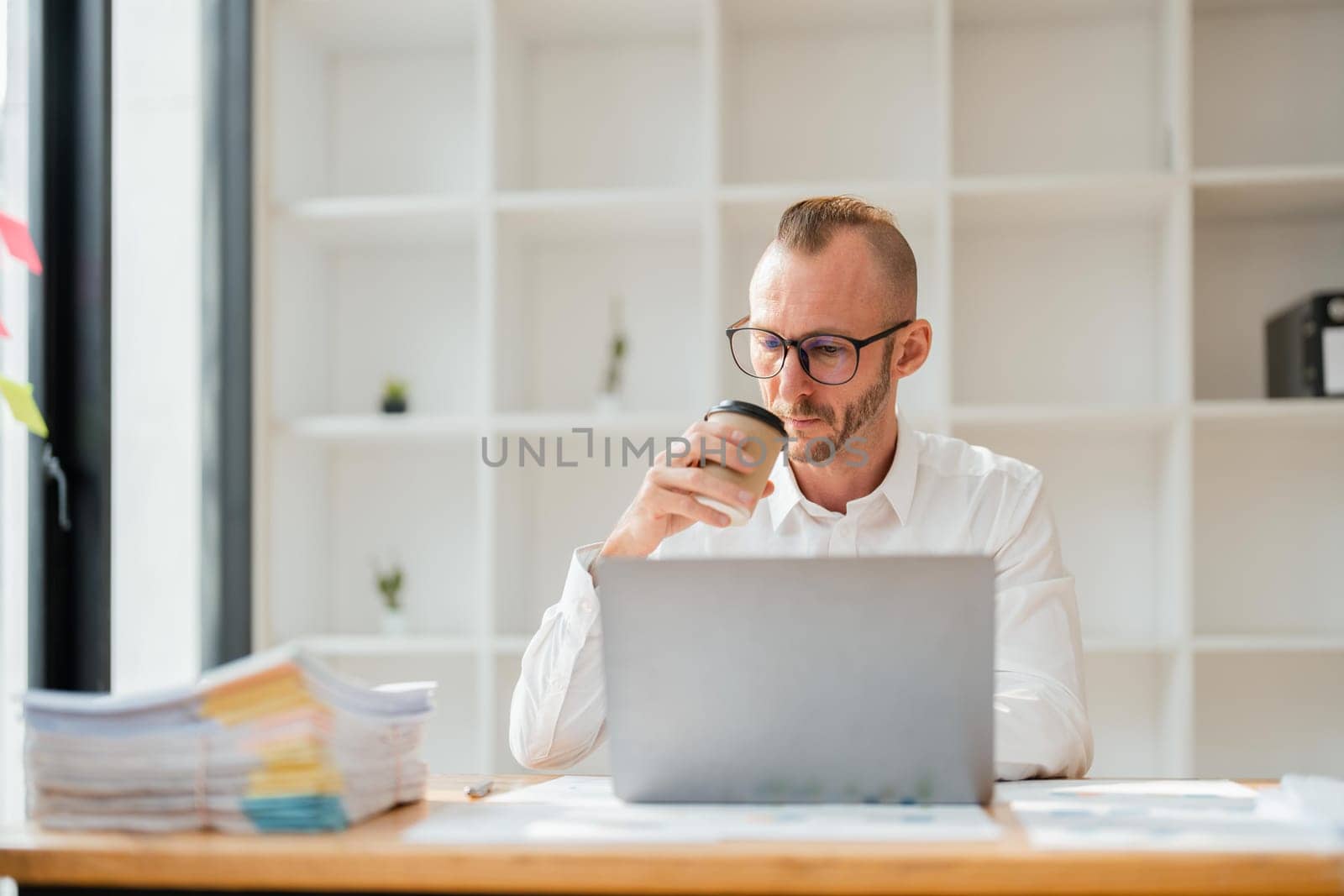 businessperson working on laptop drinking coffee at office.