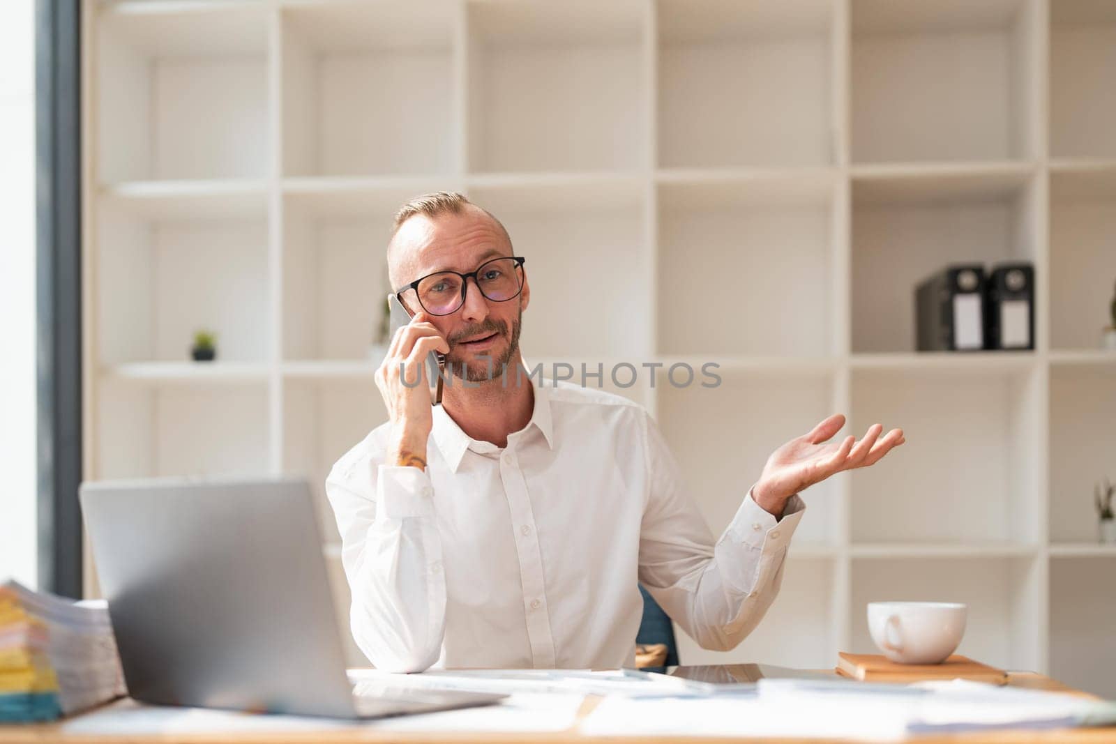 Photo of happy young businessman using laptop computer and talking on smartphone in office.