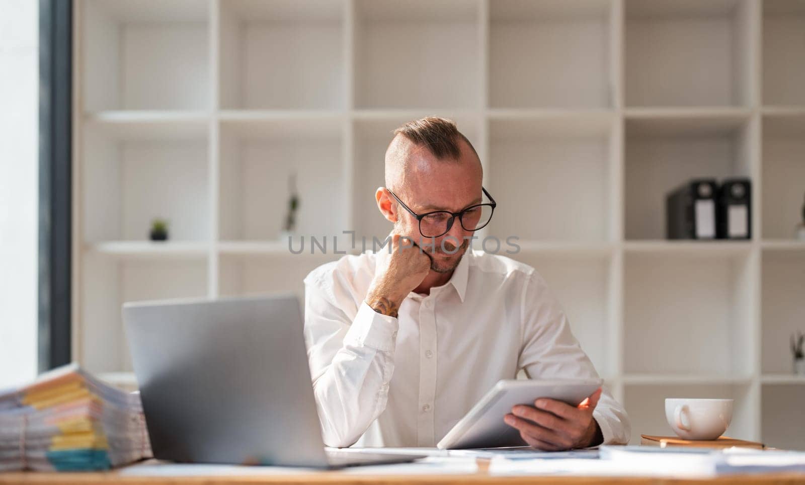 Thoughtful young businessman staring at tablet, puzzled, unsure look, distracted from analyzing tasks Have a question or challenge feel uncertain by nateemee