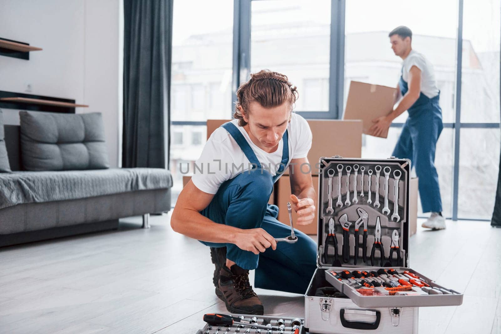 Case with equipment. Two young movers in blue uniform working indoors in the room.