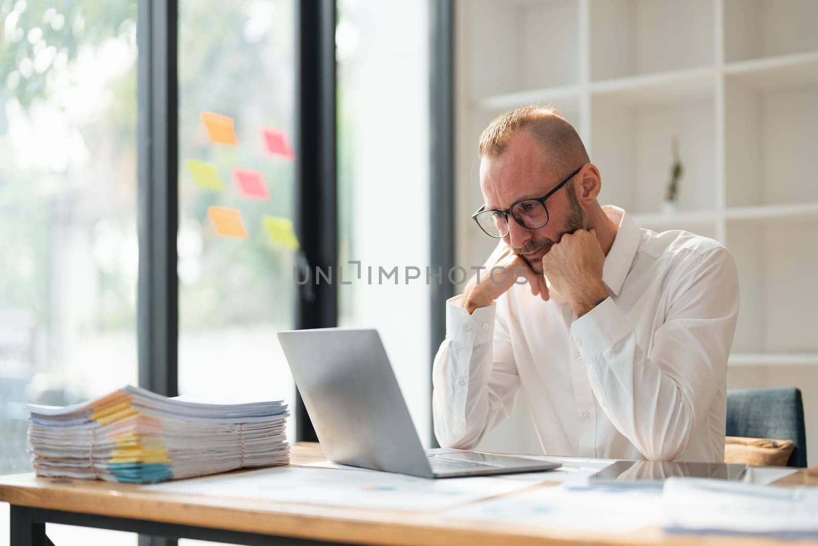 Tired businessman looking at laptop while sitting at desk in office.