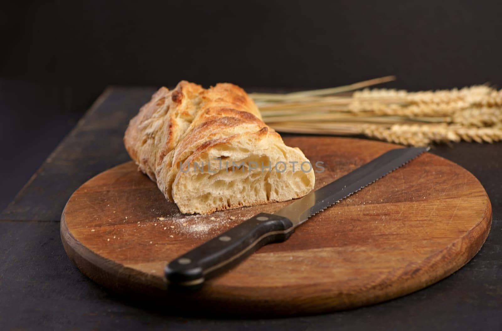 Freshly baked rye bread on a wooden board. Fresh bread on table close-up. Fresh bread on the kitchen table Whole grain bread put on kitchen wood plate with a knife for cut. by aprilphoto