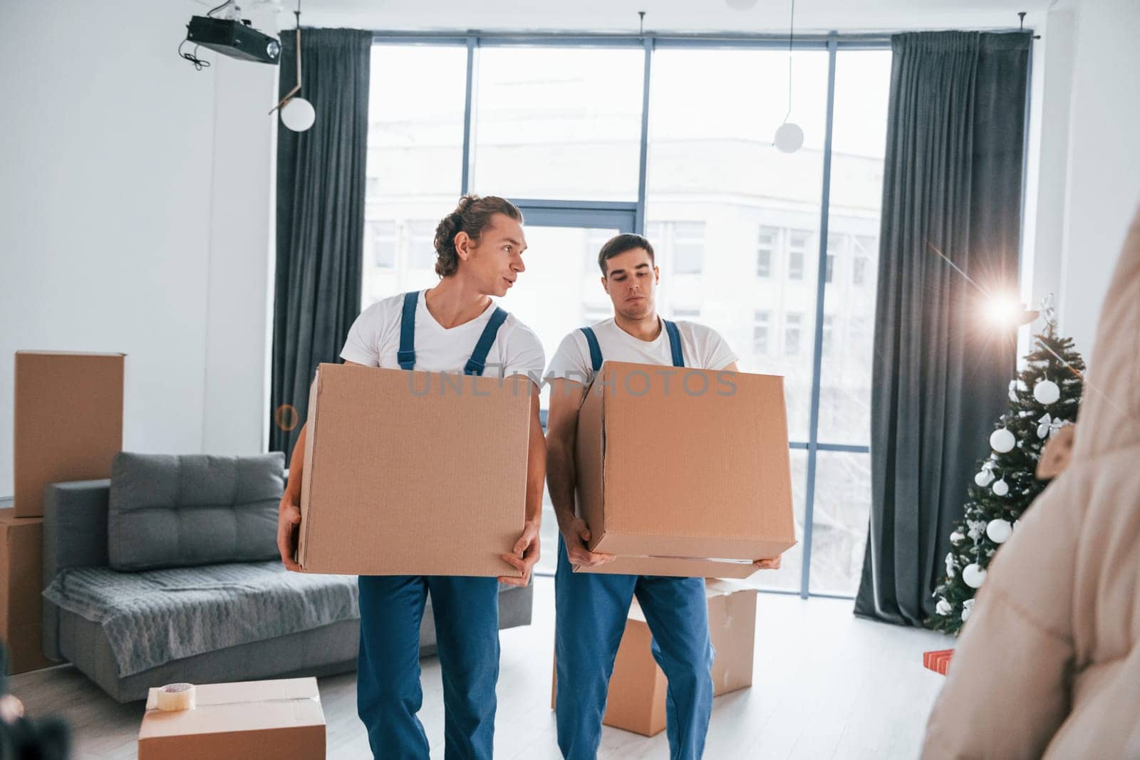 Busy day. Two young movers in blue uniform working indoors in the room.