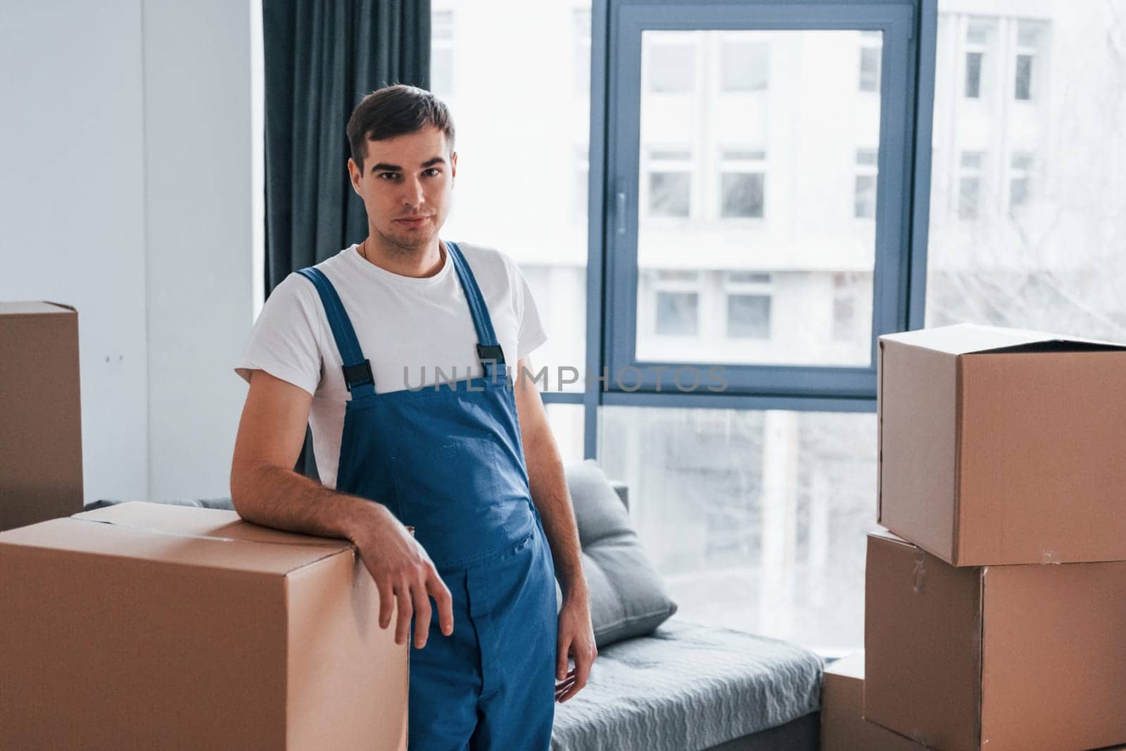 Young male mover in blue uniform works indoors in the room.