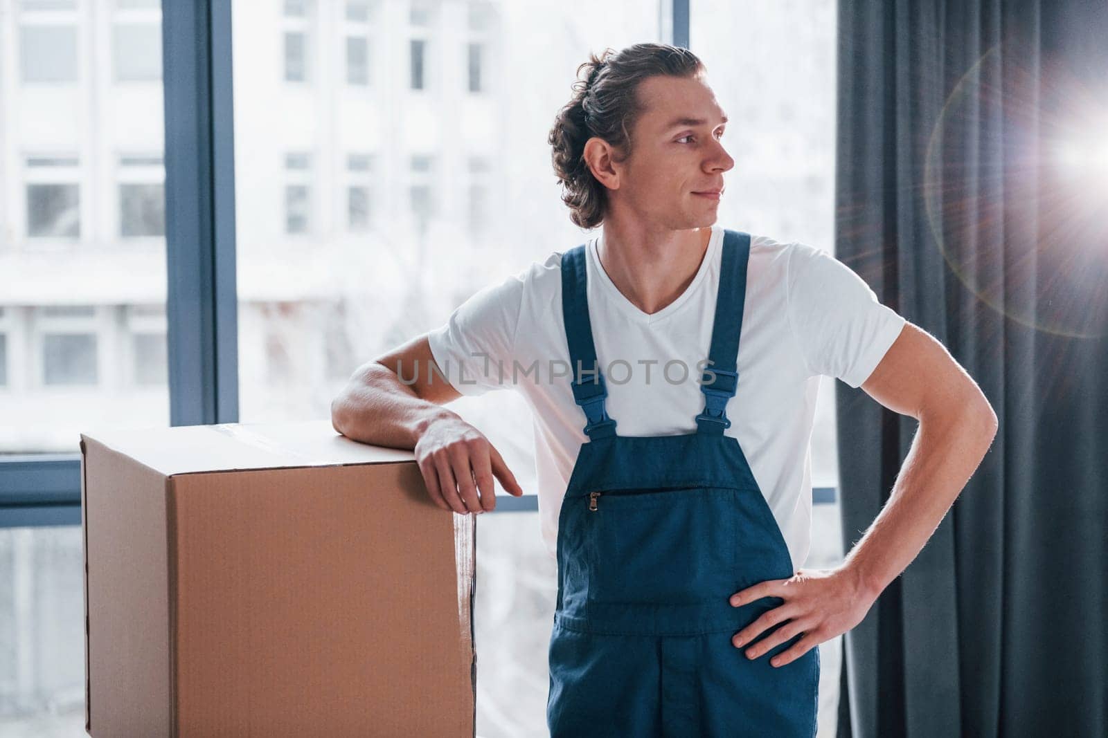 Young male mover in blue uniform works indoors in the room.