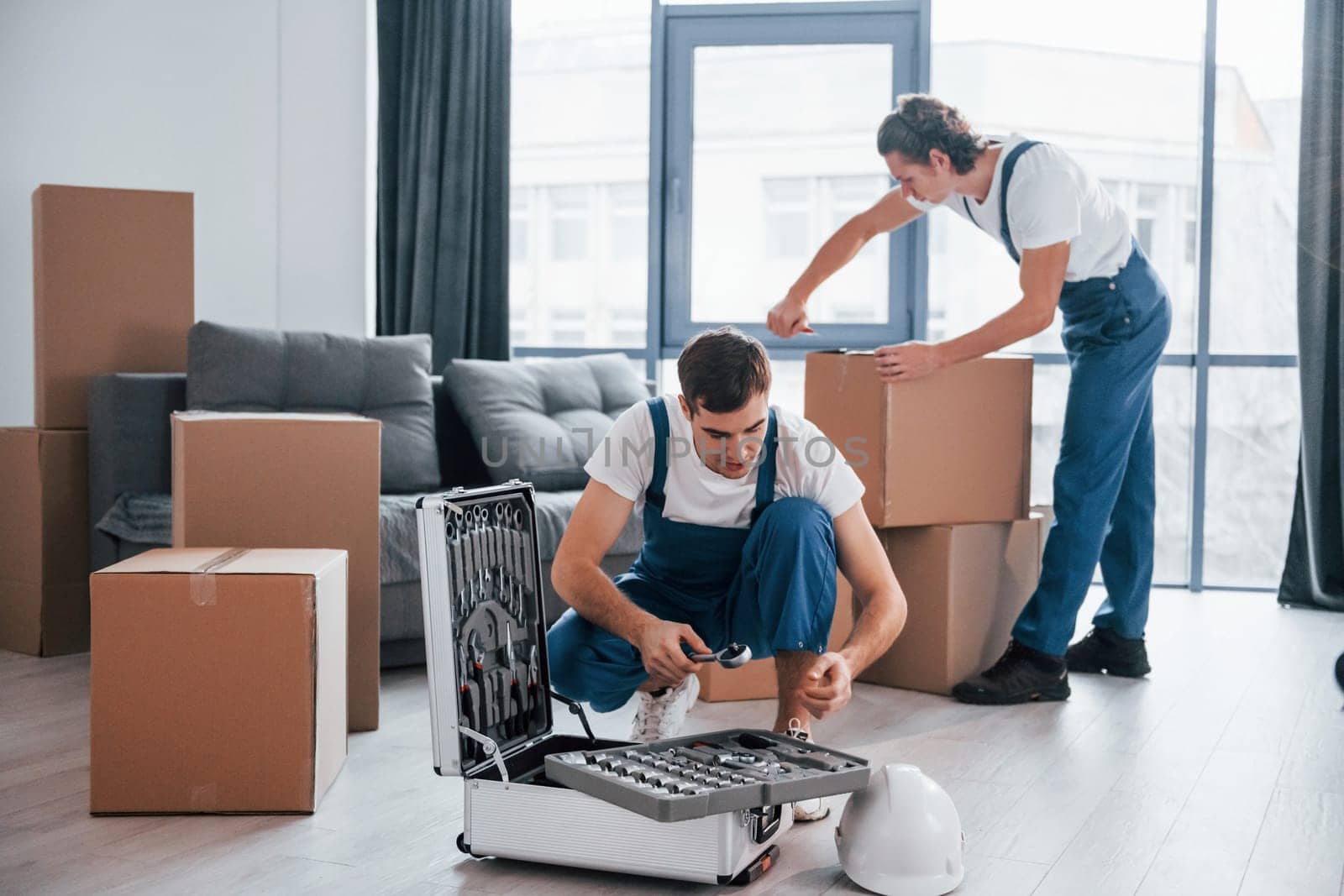 Two young movers in blue uniform working indoors in the room.