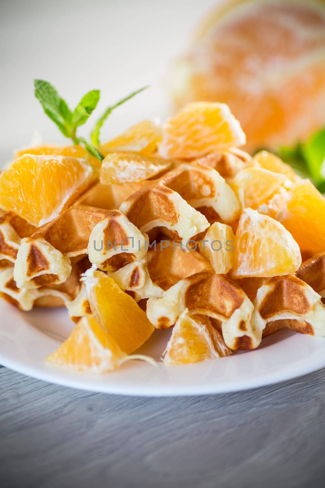 Cooked sweet Belgian waffles with oranges on a wooden table.