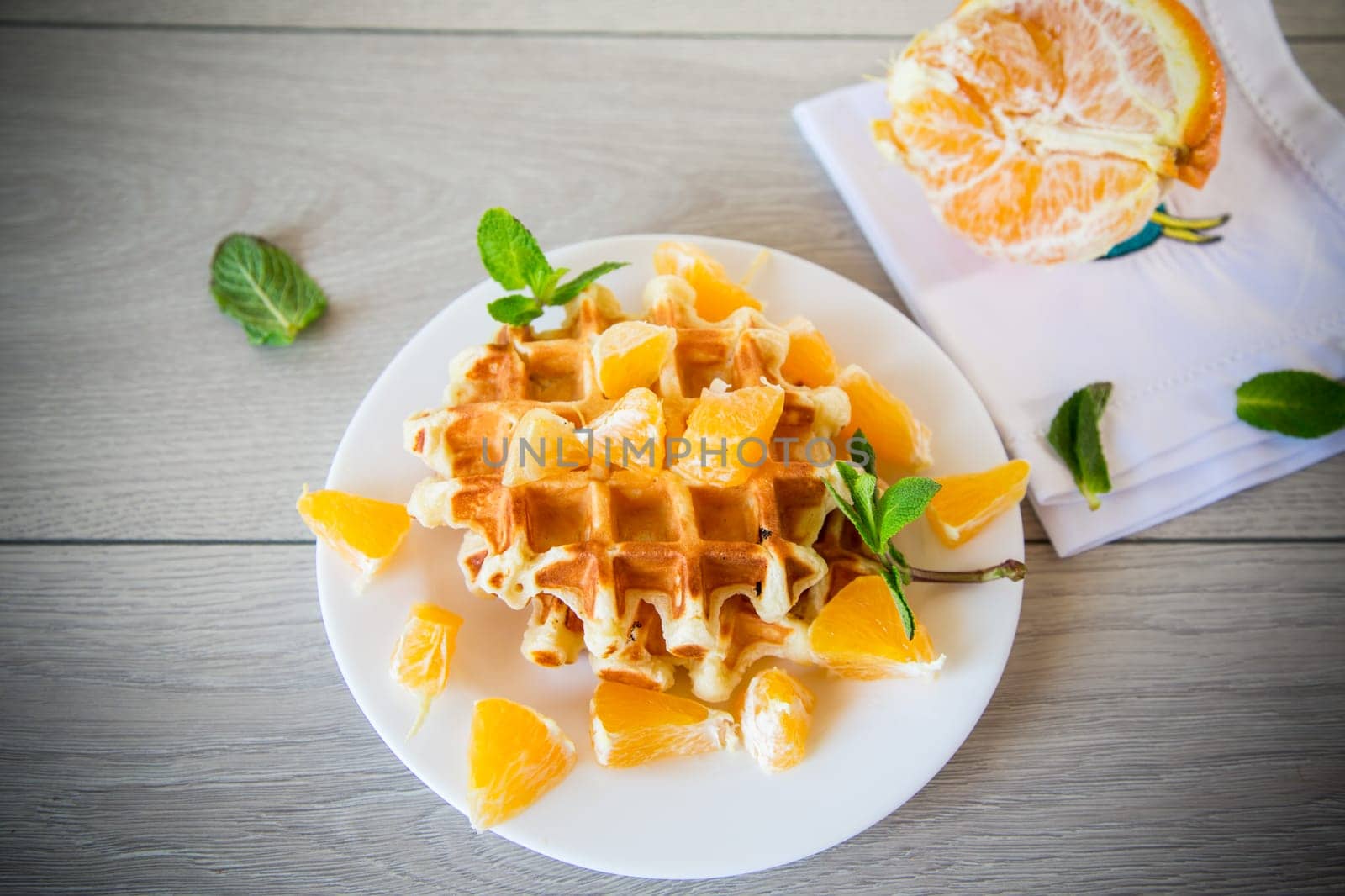 Cooked sweet Belgian waffles with oranges on a wooden table.