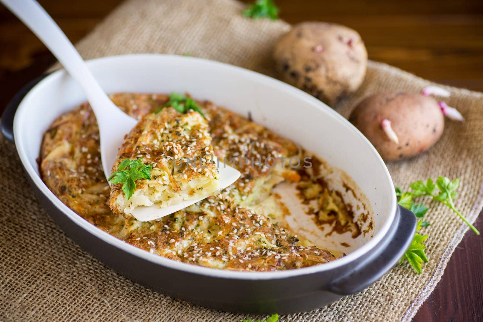 potato casserole with cabbage and spices in a ceramic form on a wooden table.
