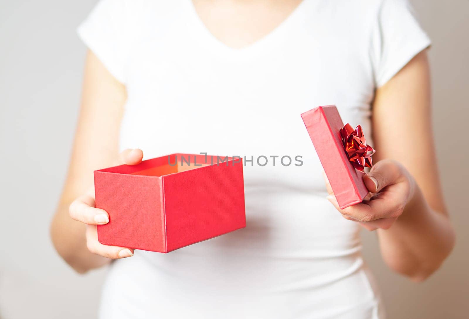Close up shot of the female hands opening a small gift in a red box.