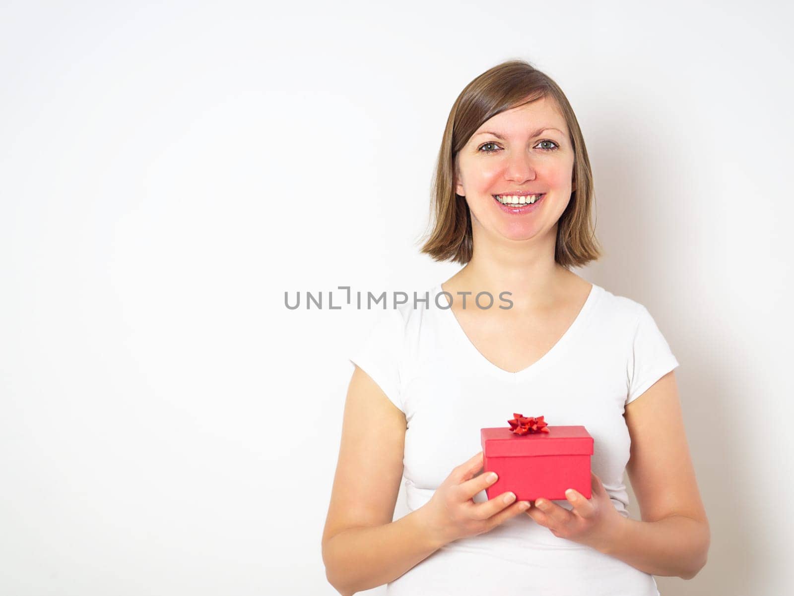 Happy attractive young woman in a white shirt holding a red gift box on the white background. High quality photo.