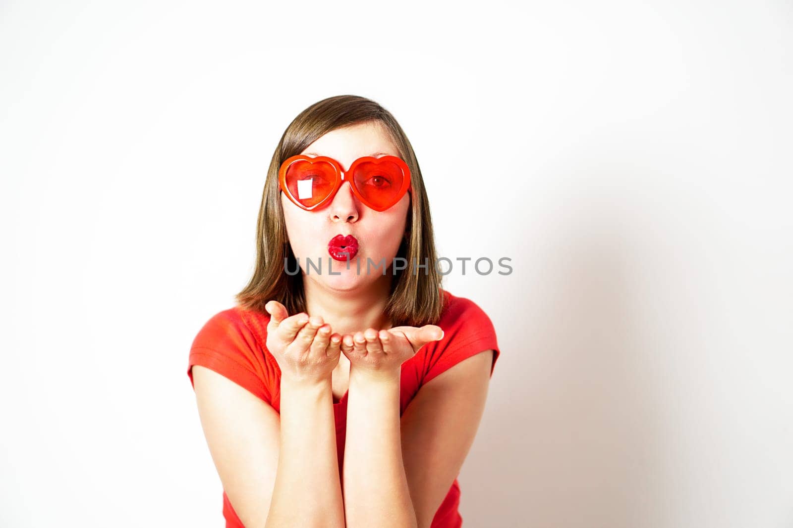 Cute lovely young woman in red heart sunglasses standing and sending an air kiss. Valentines Day. by tanjas_photoarts