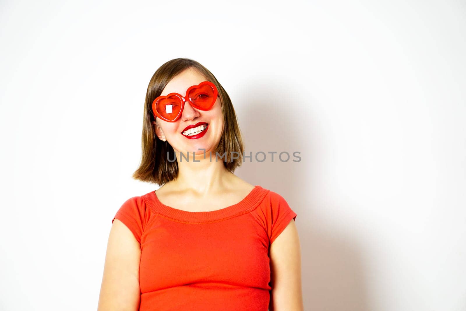 A smiling young girl in a red sunglasses and a red shirt. Valentines day. High quality photo