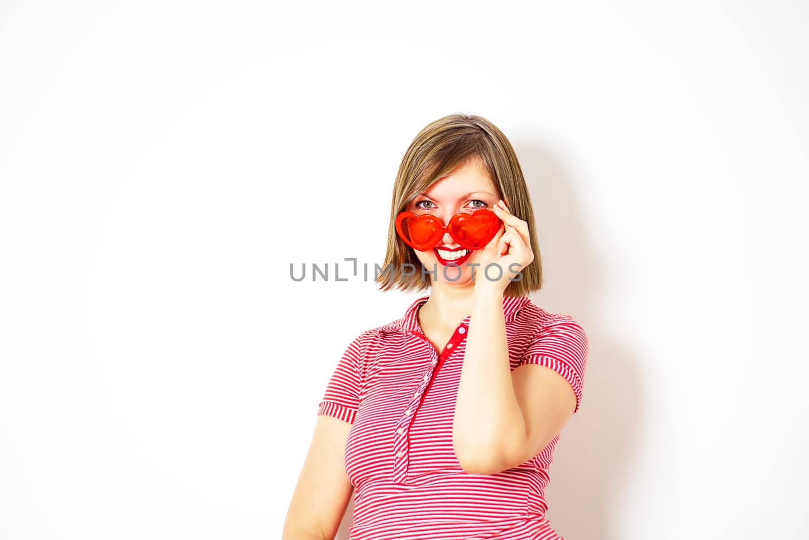 Lovely smiling young woman in red heart sunglasses standing and looking. Valentines Day concept. High quality photo.