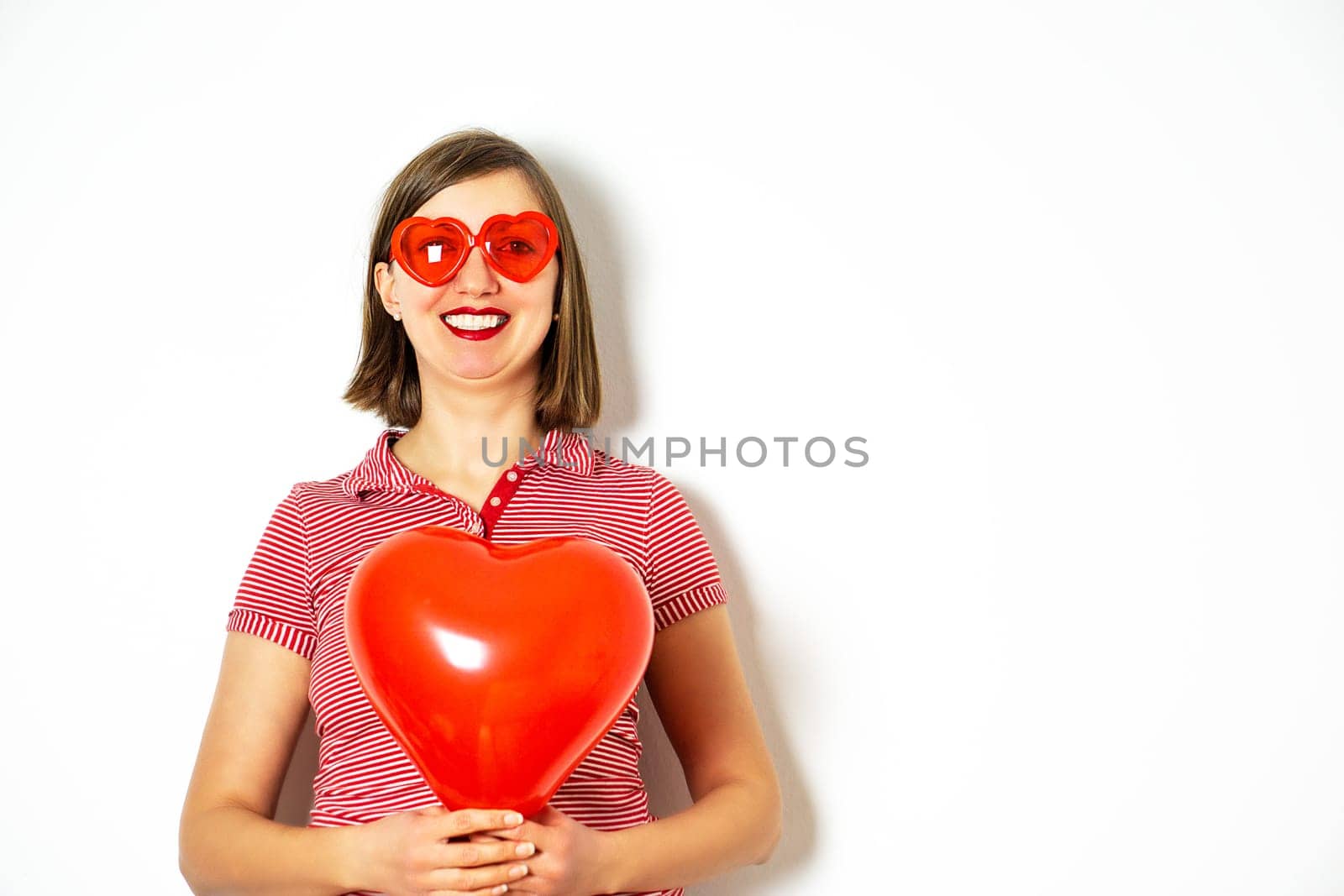 Portrait of the beautiful smiling woman in red sunglasses holding in her hand a red heart balloon for Valentines Day. High quality photo