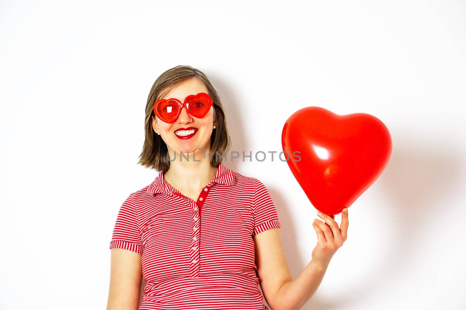 Beautiful smiling woman in red sunglasses holding in her hand a red heart balloon for Valentines Day. High quality photo