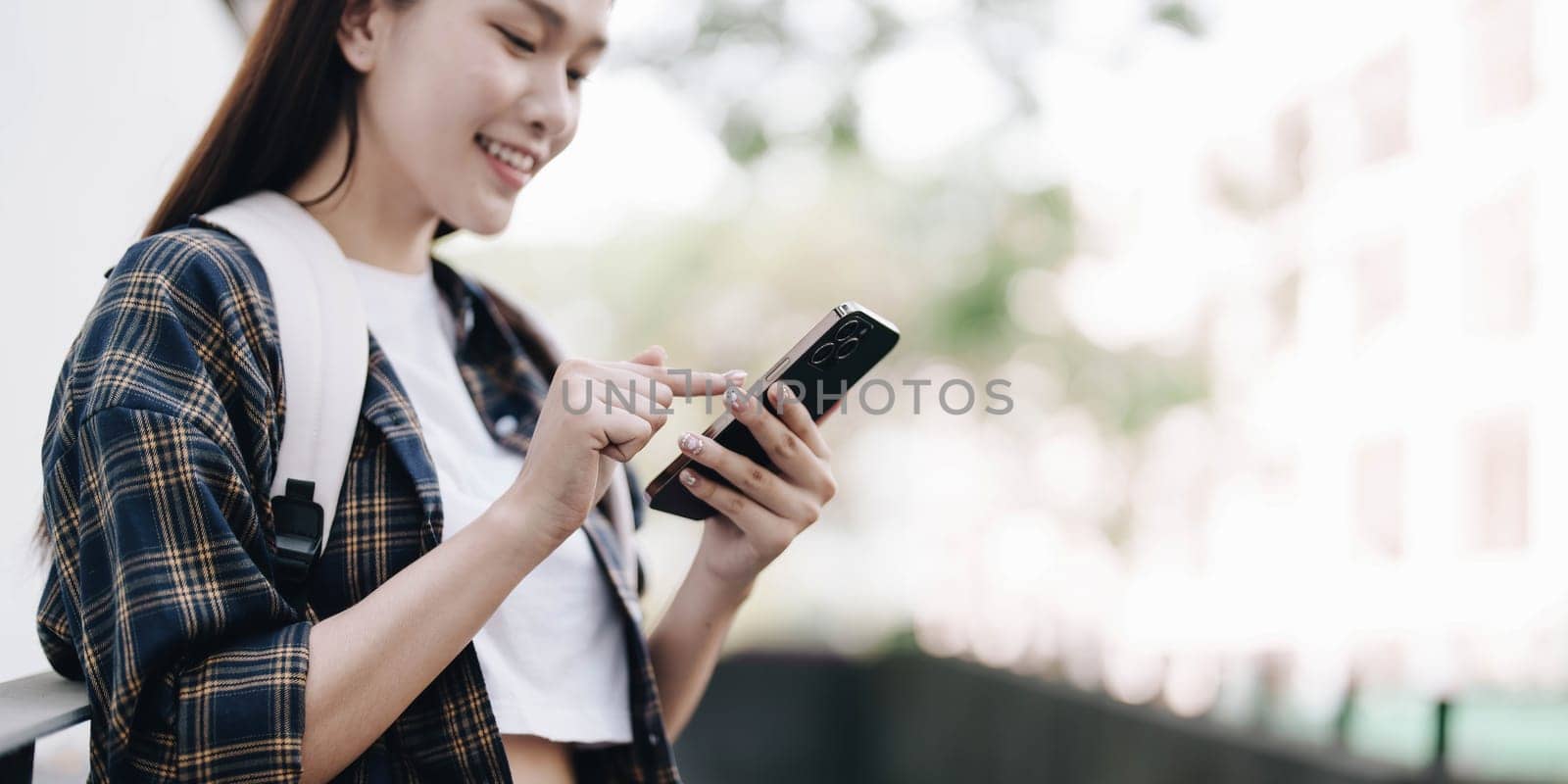 One happy student walking and using smart phone on line in the street at sunset with a warm back light..