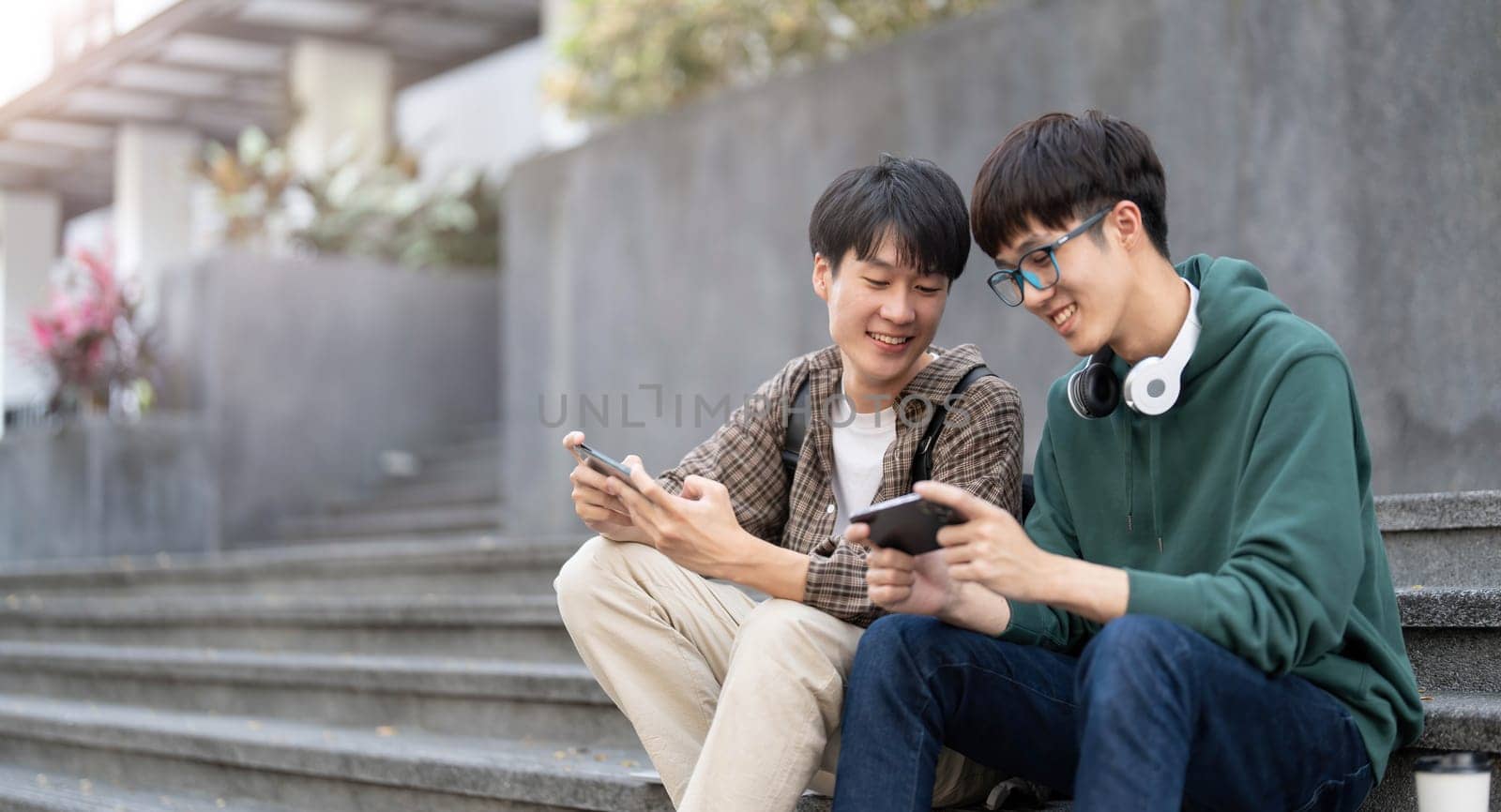 Happy Asian man college student playing mobile game on his smartphone with his friend..