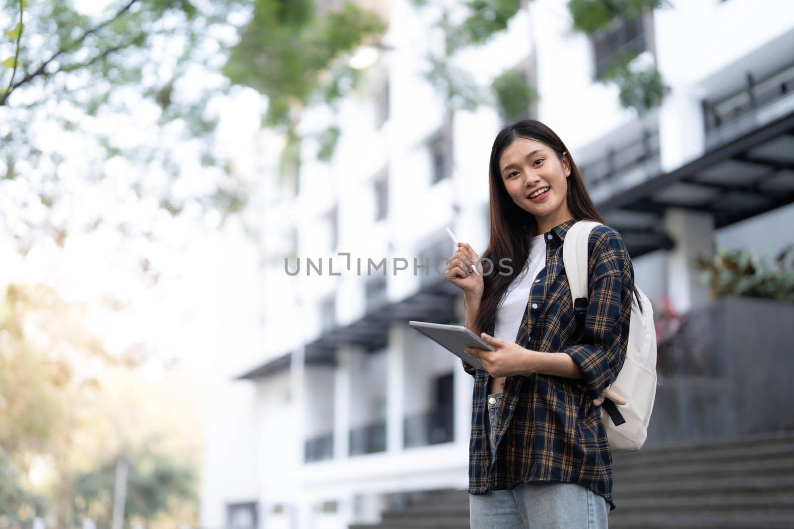 Female college students happily holding laptops outdoors after school on campus. when the sun goes down the horizon with warm light by wichayada