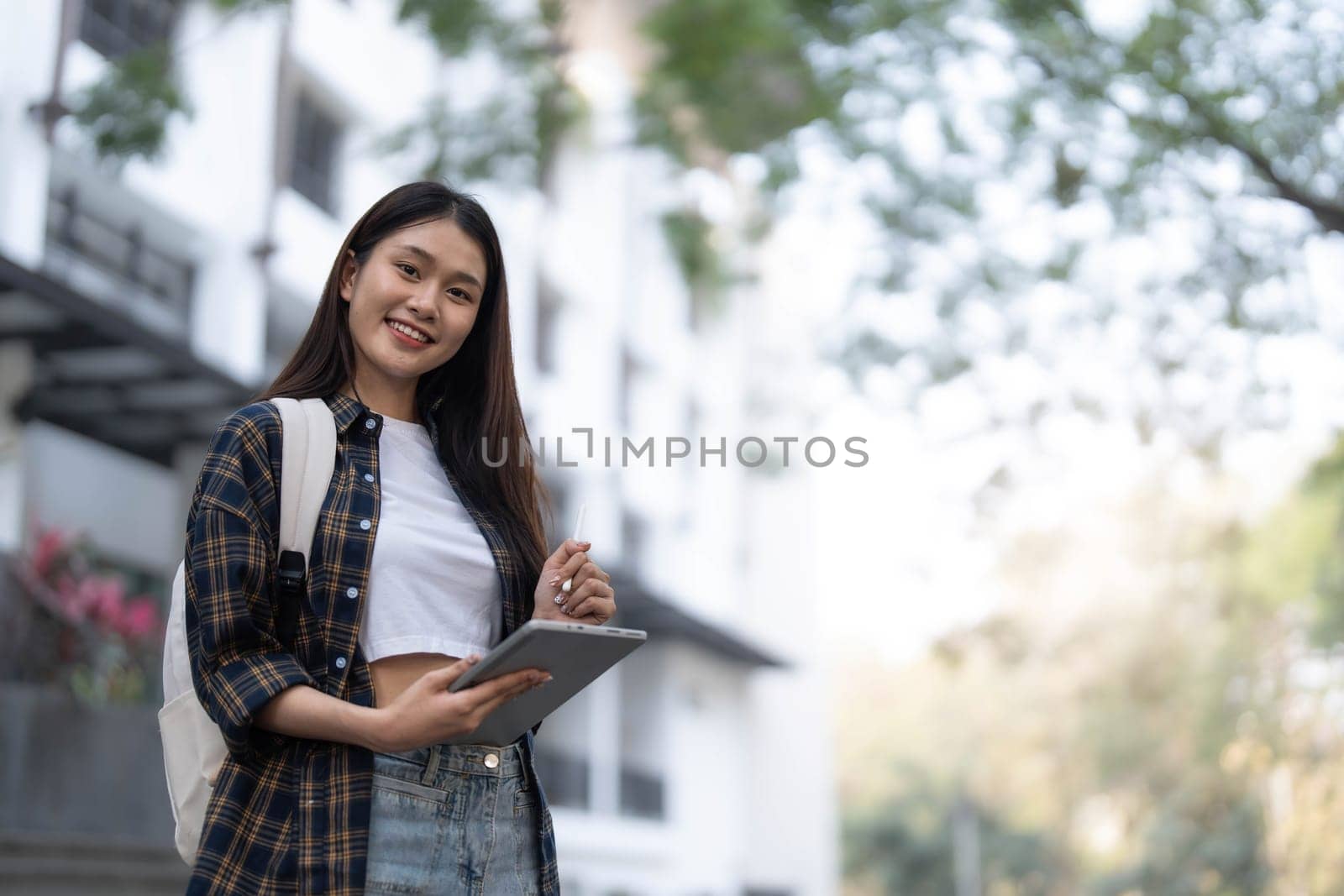 Female college students happily holding laptops outdoors after school on campus. when the sun goes down the horizon with warm light by wichayada