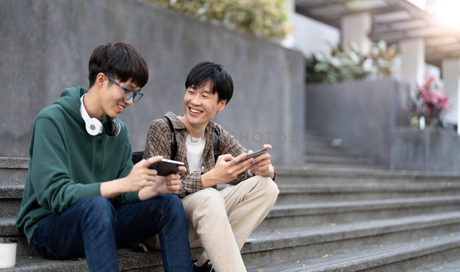 Happy Asian man college student playing mobile game on his smartphone with his friend by wichayada