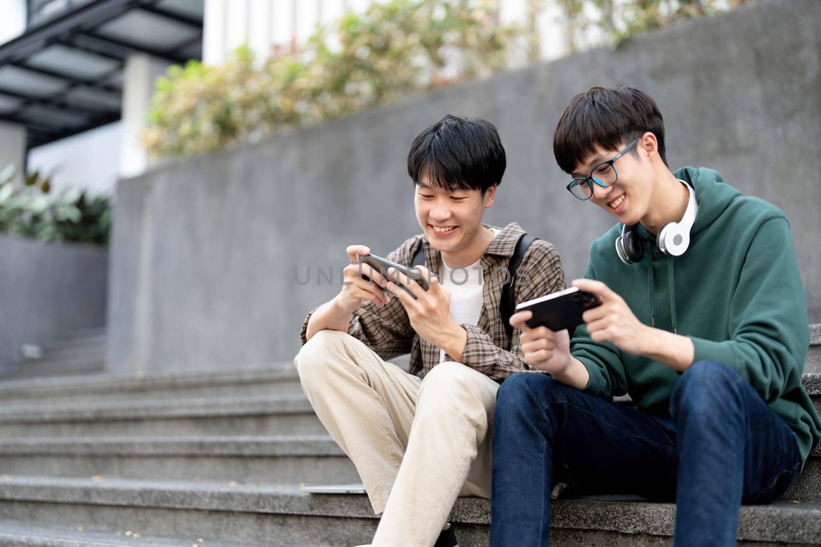 Happy Asian man college student playing mobile game on his smartphone with his friend..