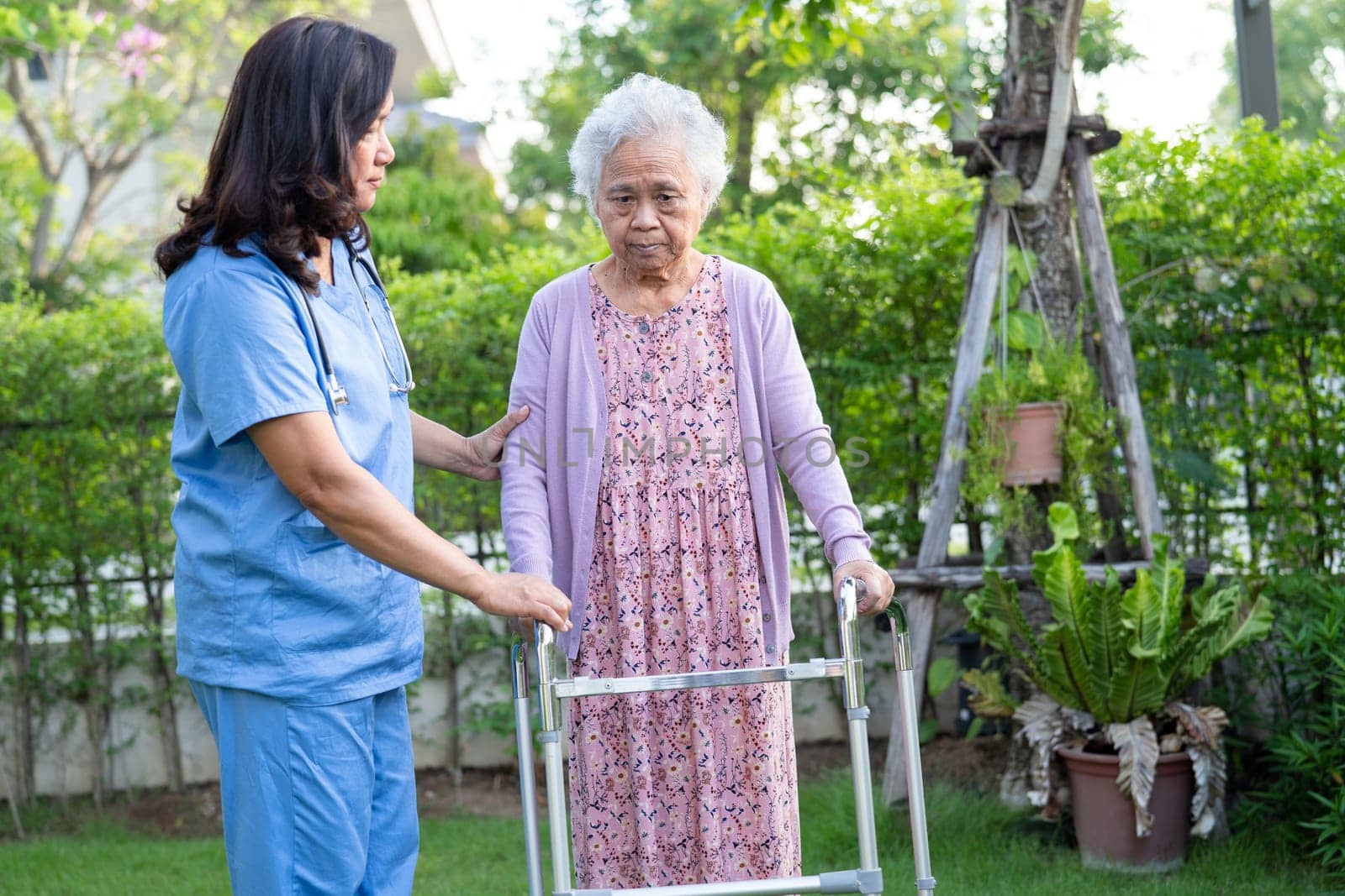 Doctor caregiver help and care Asian senior woman patient walk with walker in park at hospital. by pamai