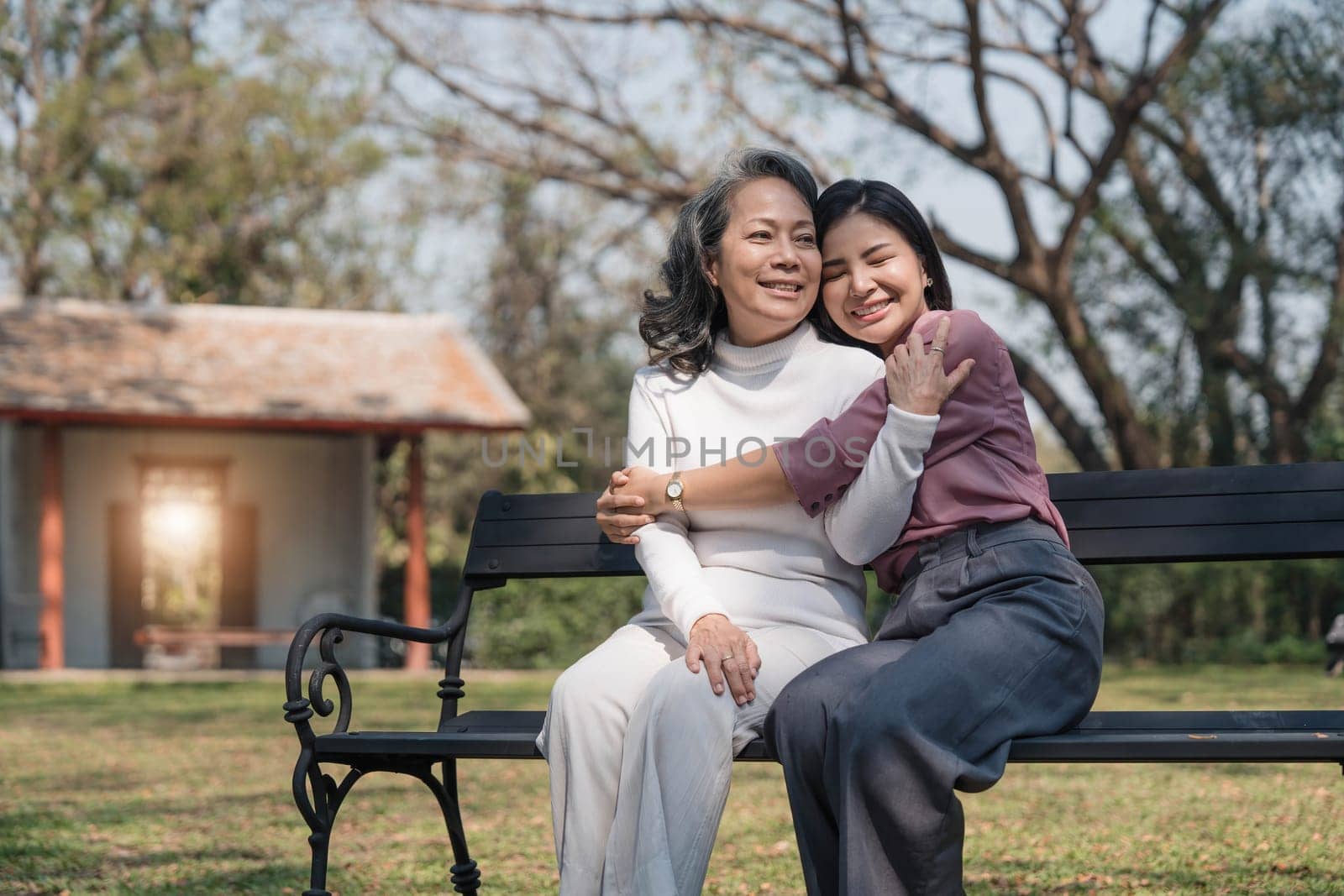 Happy adult granddaughter and senior grandmother having fun enjoying talk sit with green nature. in park by wichayada