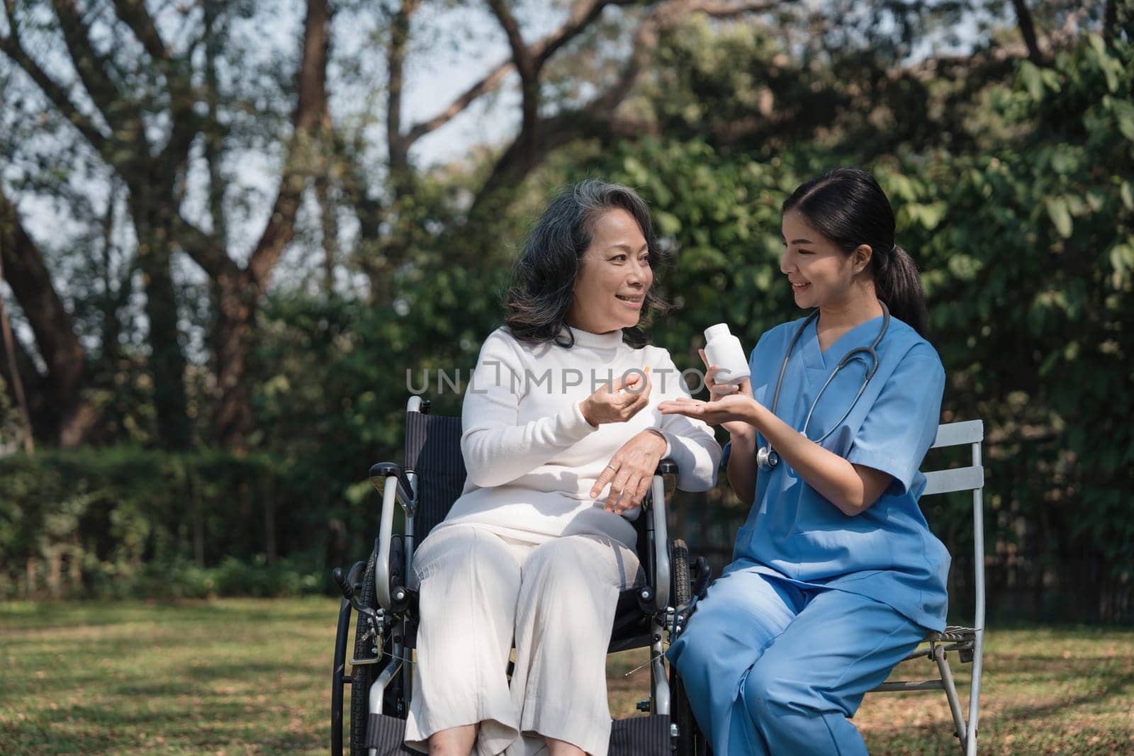 Female nurse doing blood pressure measurement of a senior woman patient. Doctor checking blood pressure of an elderly woman at garden home. Female caregiver and senior woman together